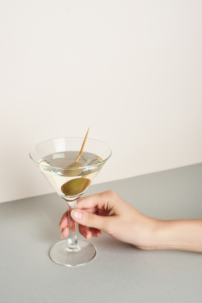 Widok kobiety trzymającej koktajl martini na szarej powierzchni na białym tle - Zdjęcie, obraz