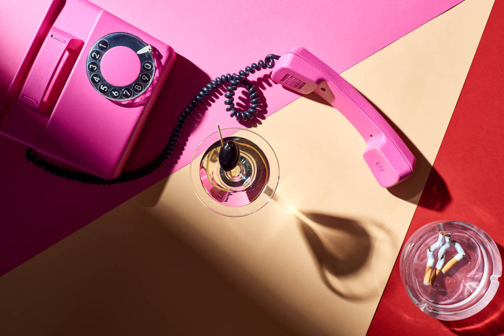Widok z góry zabytkowy telefon z martini w szkle i popielniczka z niedopałkami papierosów na kolorowe powierzchni - Zdjęcie, obraz