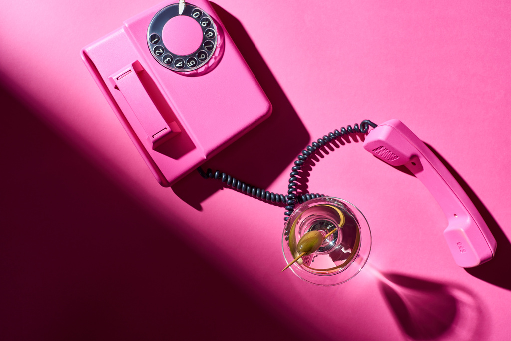 Vue du dessus du martini en verre avec téléphone rétro sur fond rose
 - Photo, image