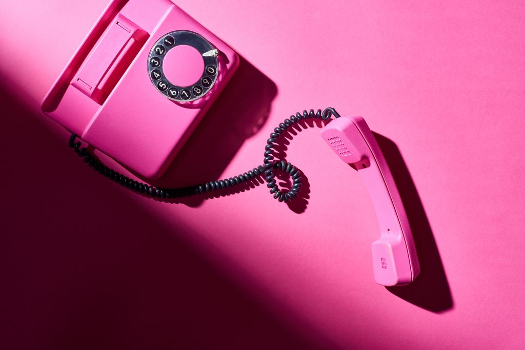 Vista superior del teléfono rosa vintage con sombra en la superficie brillante
 - Foto, Imagen