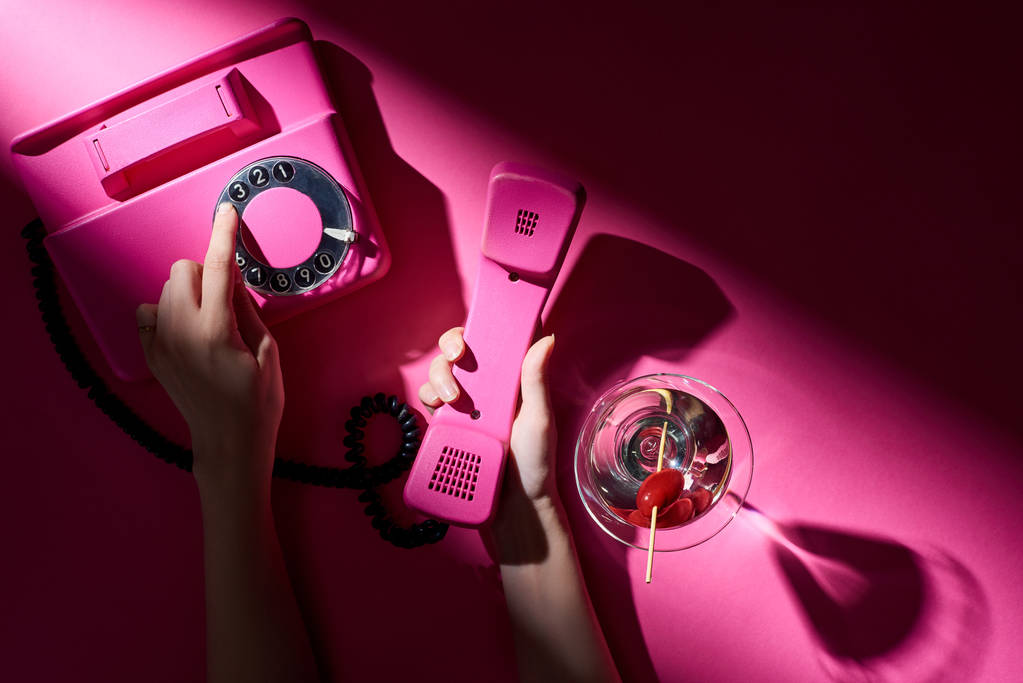 Oříznutý pohled na ženu pomocí vintage telefon vedle koktejlu na růžovém pozadí - Fotografie, Obrázek