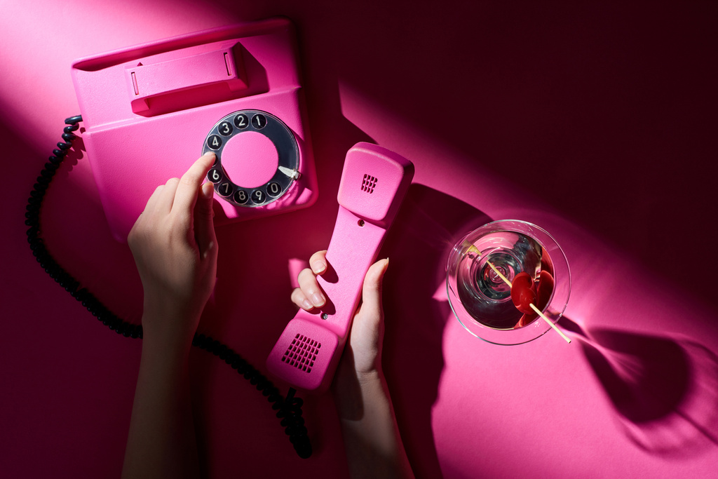 Gesneden weergave van de vrouw met behulp van retro telefoon met martini naast op roze achtergrond - Foto, afbeelding