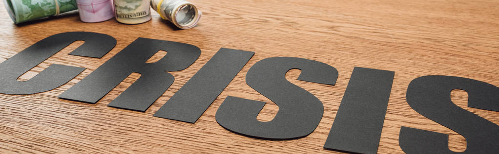 tiro panorâmico de papel preto cortar crise palavra perto de rolos de dinheiro na superfície de madeira
 - Foto, Imagem
