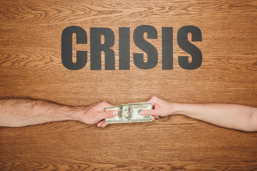 osittainen näkymä miehestä ja naisesta, joilla on dollarin seteli lähellä mustaa paperia leikattu sana kriisi puupinnalla
 - Valokuva, kuva