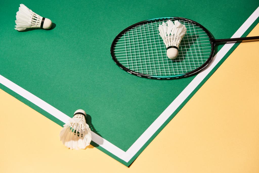 Hoge hoek weergave van badminton racket en shuttlecocks op groene baan op geel oppervlak - Foto, afbeelding