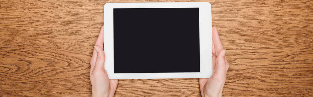Ausgeschnittene Ansicht einer Frau, die ein digitales Tablet mit leerem Bildschirm auf einem Holztisch hält, Panoramaaufnahme - Foto, Bild