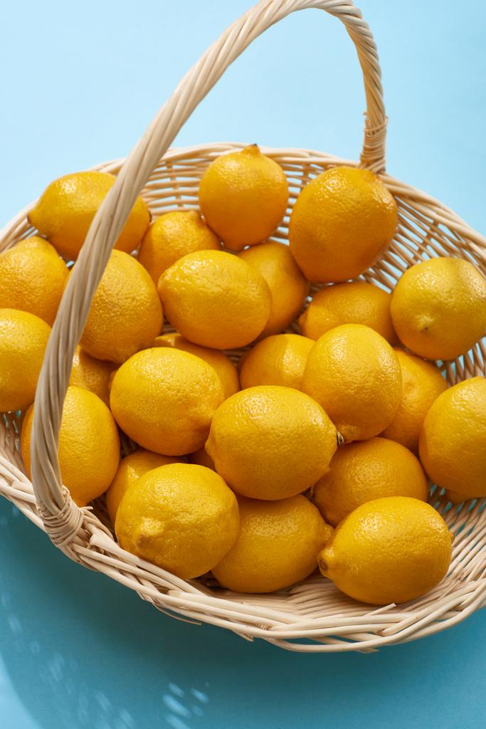 citrons jaunes mûrs dans un panier en osier sur fond bleu
 - Photo, image