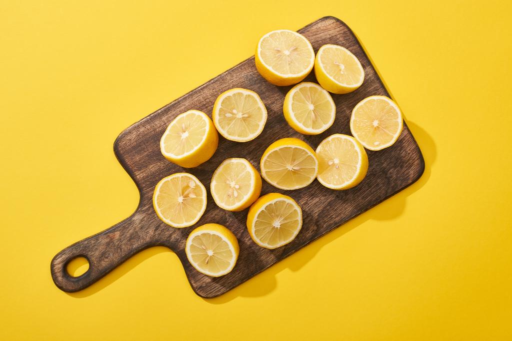 bovenaanzicht van rijpe gesneden citroenen op houten snijplank op gele achtergrond - Foto, afbeelding