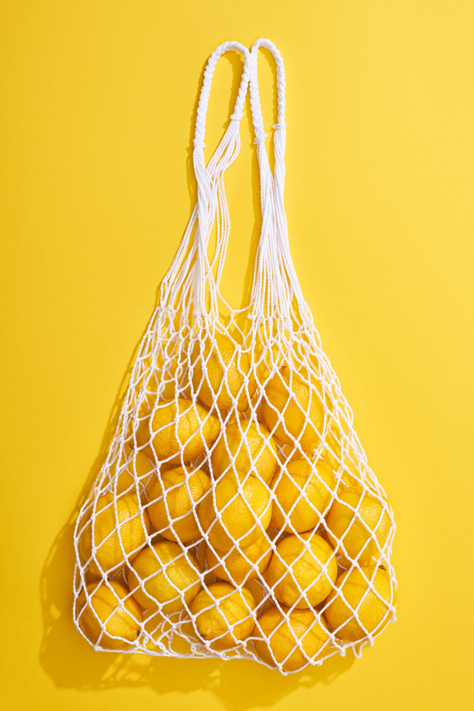黄色の背景のエコストリングバッグの中の新鮮な熟した全レモンのトップビュー - 写真・画像