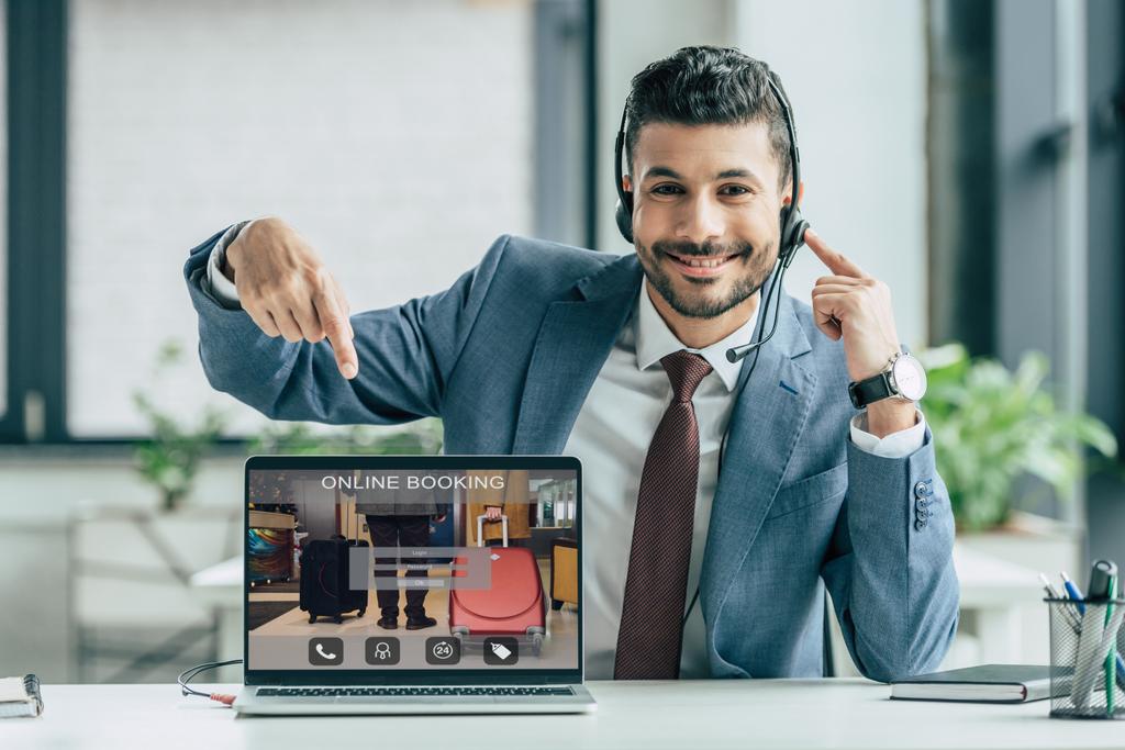 operador de call center alegre apontando com o dedo para laptop com site de reservas on-line na tela
 - Foto, Imagem