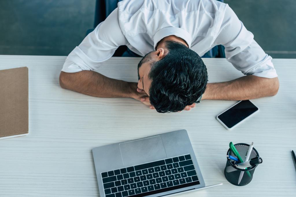 horní pohled vyčerpaného podnikatele spícího na pracovišti v blízkosti notebooku a smartphonu - Fotografie, Obrázek