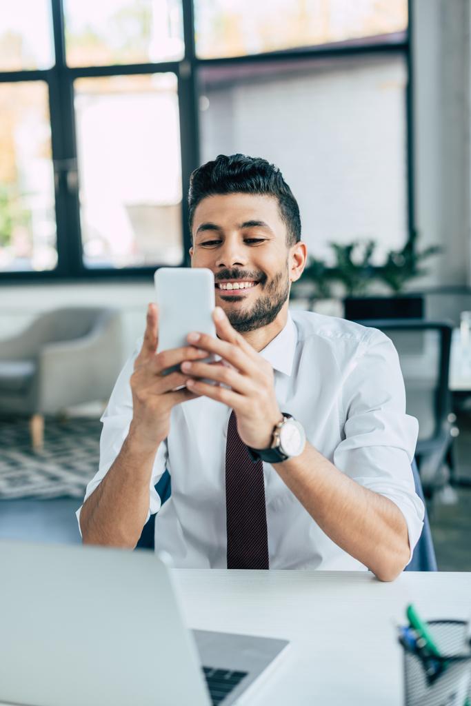 вибірковий фокус веселого бізнесмена за допомогою смартфона сидячи на робочому місці
 - Фото, зображення