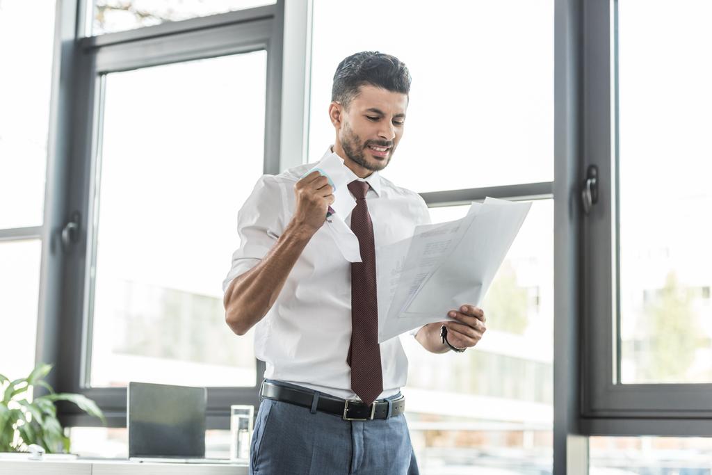 dissatisfied businessman crumpling paper while standing near window in office - Photo, Image