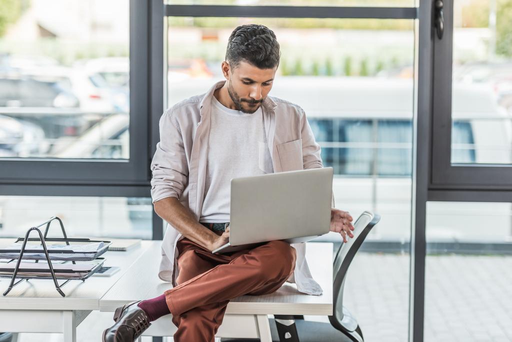 junger Geschäftsmann in lässiger Kleidung am Schreibtisch sitzend und mit Laptop - Foto, Bild