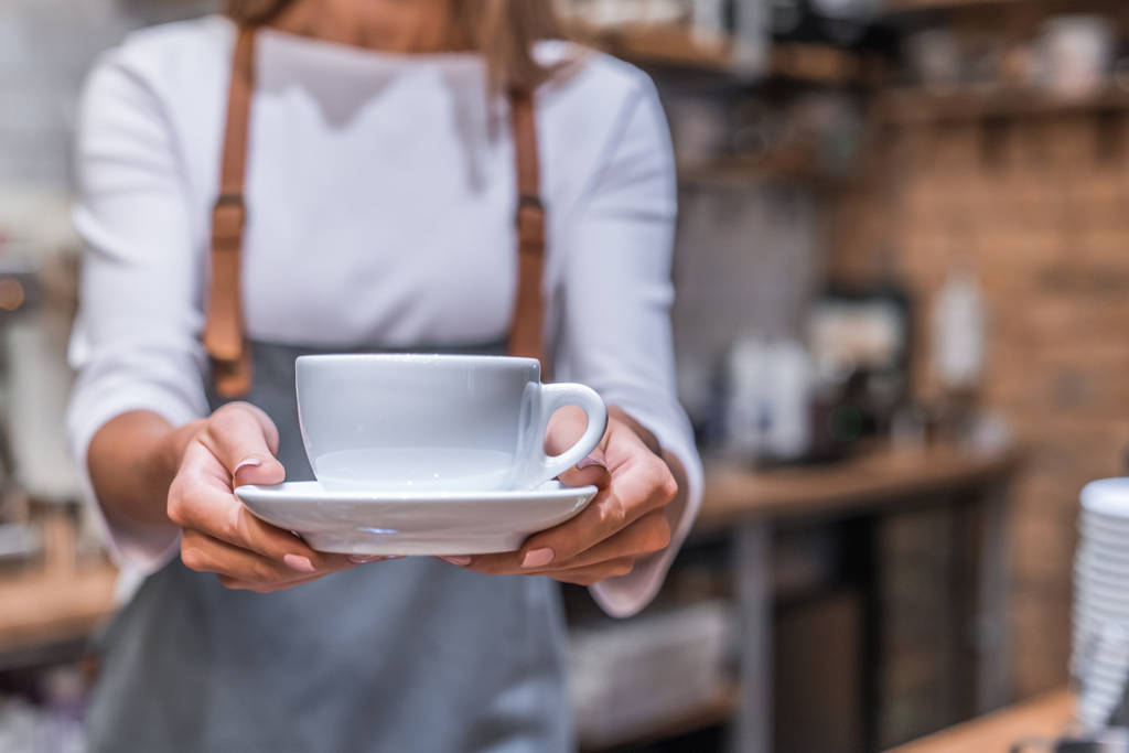 Jonge vrouw barista houden koffie kopje serveren klant in coffeeshop - Foto, afbeelding
