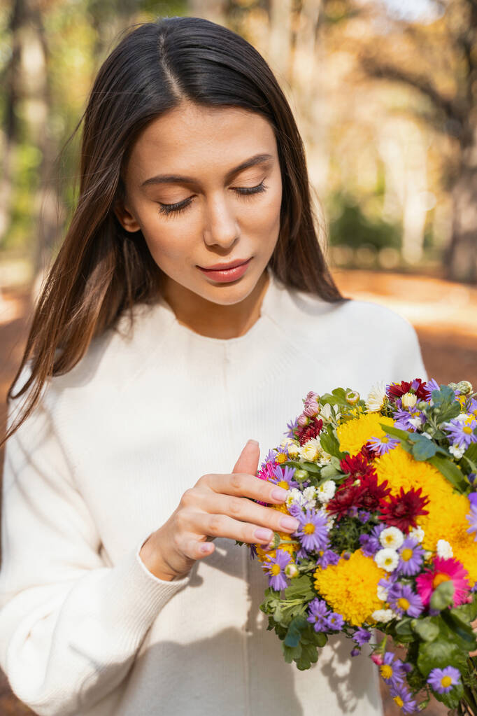 Kaunis nainen koskettaa kukkia käsissään
 - Valokuva, kuva