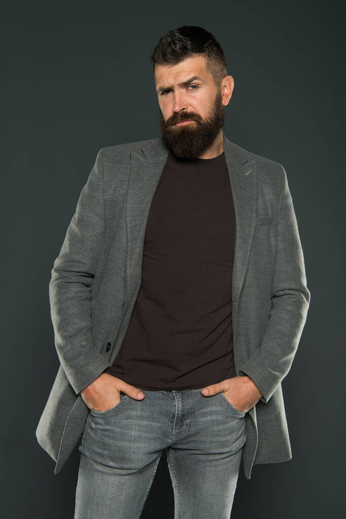 Bearded and barbate. Bearded man keeping arms in pockets on grey background. Bearded hipster in casual style. Brutal unshaven guy wear mustache and beard on bearded face - Photo, Image