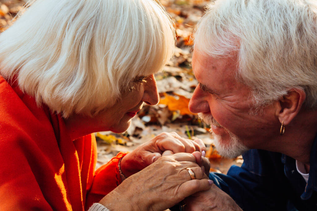 Κοντινό πορτραίτο ενός ευτυχισμένου γέρου που φιλάει τα χέρια της γυναίκας του. Στο πάρκο το φθινόπωρο ένα ευτυχισμένο ζευγάρι ξεκουράζεται.. - Φωτογραφία, εικόνα