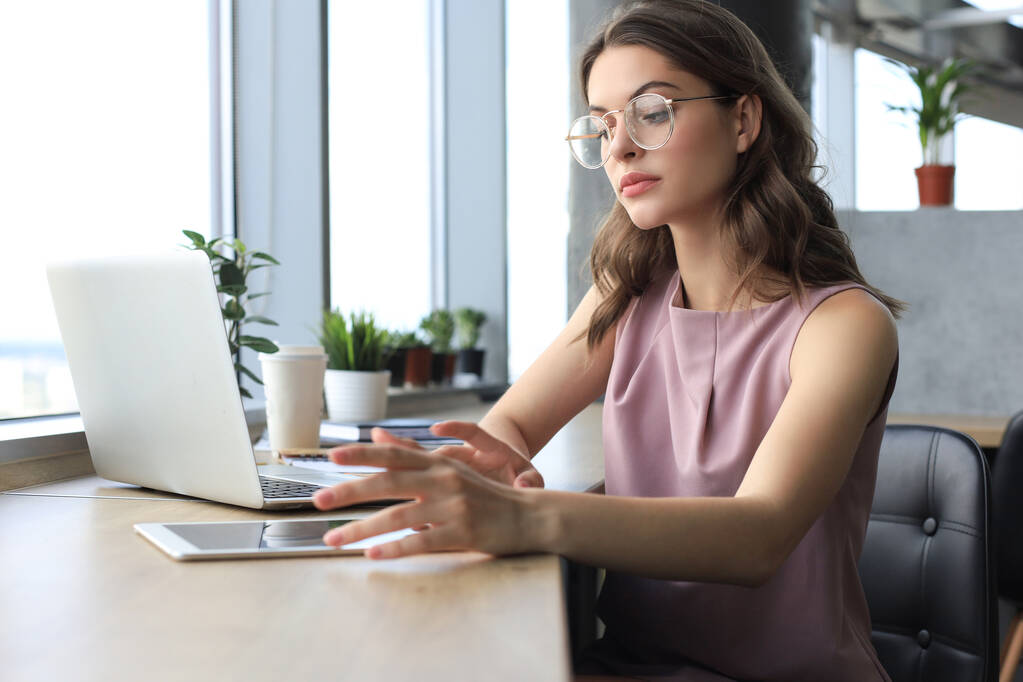 Красивая деловая женщина в элегантной повседневной одежде работает на ноутбуке в офисе - Фото, изображение