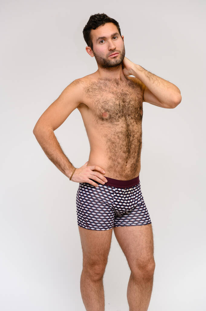 Porträt eines hübschen männlichen Modells mit perfektem Körper, nackt in kurzen Hosen stehend, posierend auf weißem Hintergrund. schwarze Haare. Studioaufnahme aus der Nähe - Foto, Bild