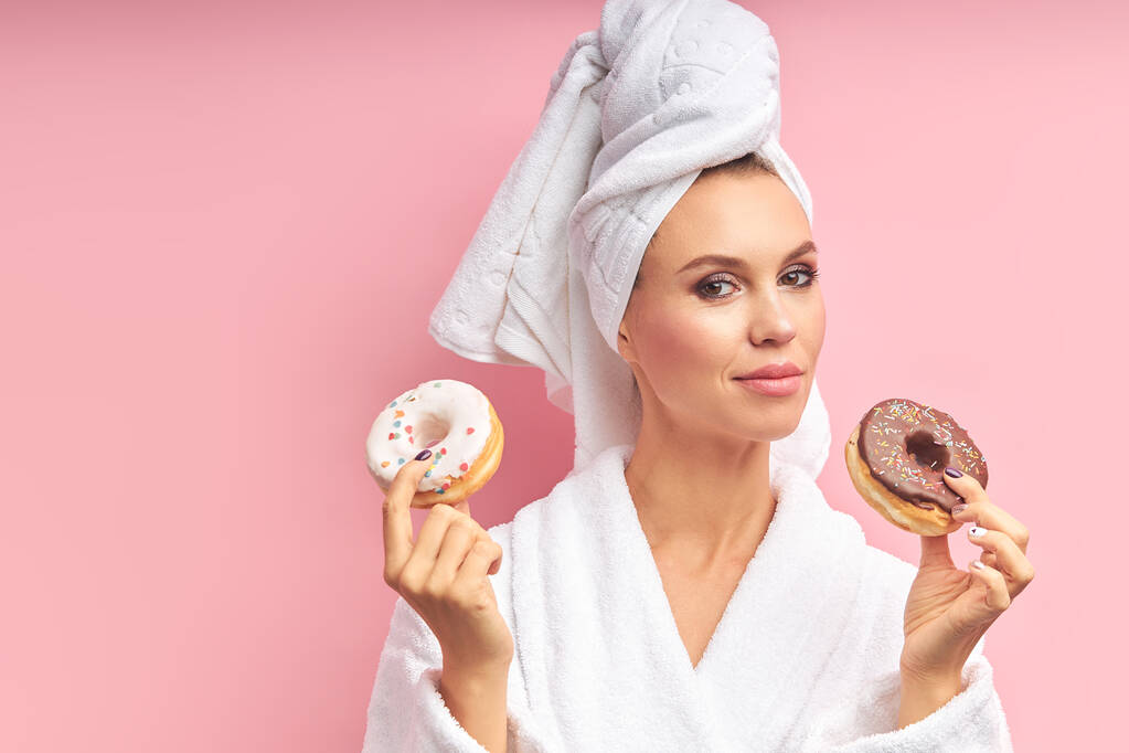 Запутавшаяся красивая женщина с полотенцем на волосах, держа пончики, выбирай
 - Фото, изображение