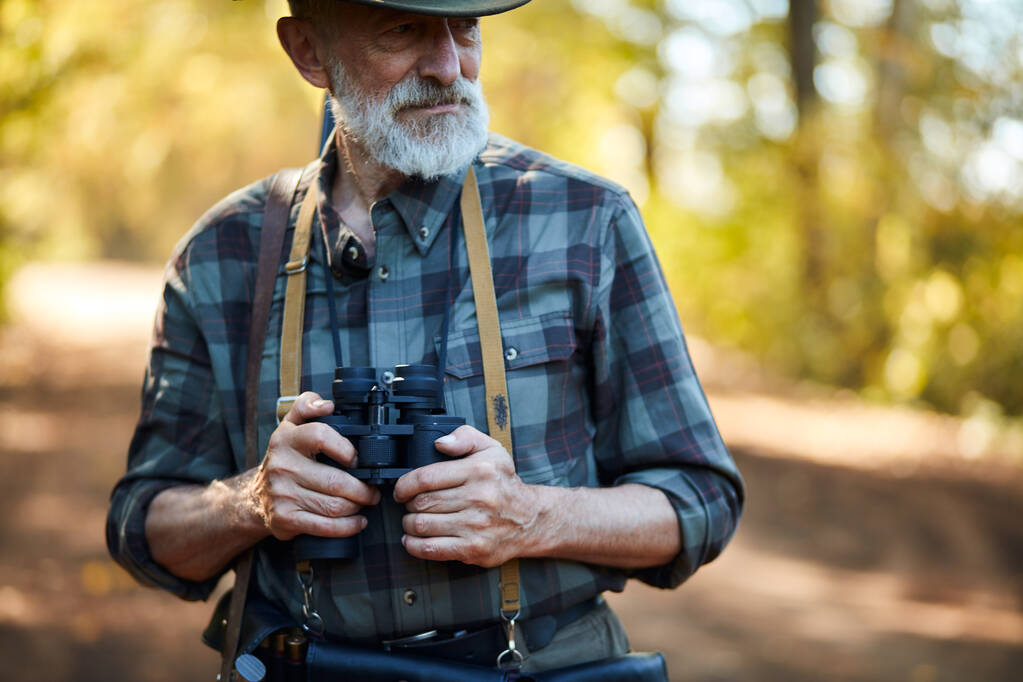 Az idősebb szakállas vadász távcsövet használ. - Fotó, kép