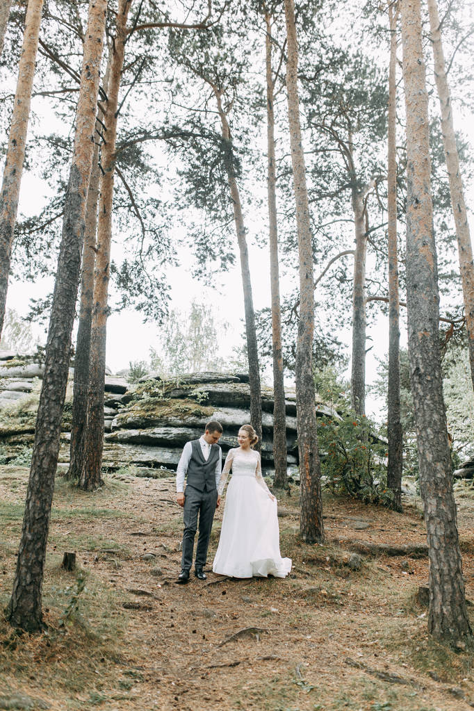 Moderne ceremonie in Europese stijl. Mooi bruidspaar in sfeervol bos met rotsen.  - Foto, afbeelding