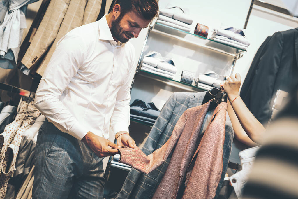 Muž si vybere mezi dvěma bundami v obchodě s oblečením - Fotografie, Obrázek