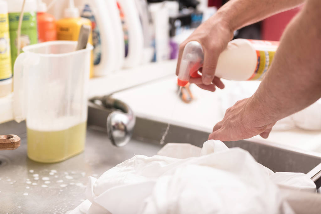 руки мужчины стирают грязную одежду специальным пятновыводителем
 - Фото, изображение