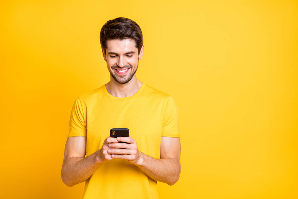 Photo of amazing handsome guy holding telephone hands chatting with friends discussing future chill students party wear casual t-shirt isolated yellow color background - Photo, Image