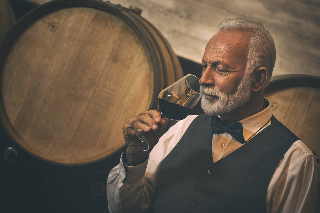 Старший мужчина с бородой держит бокал красного вина
  - Фото, изображение