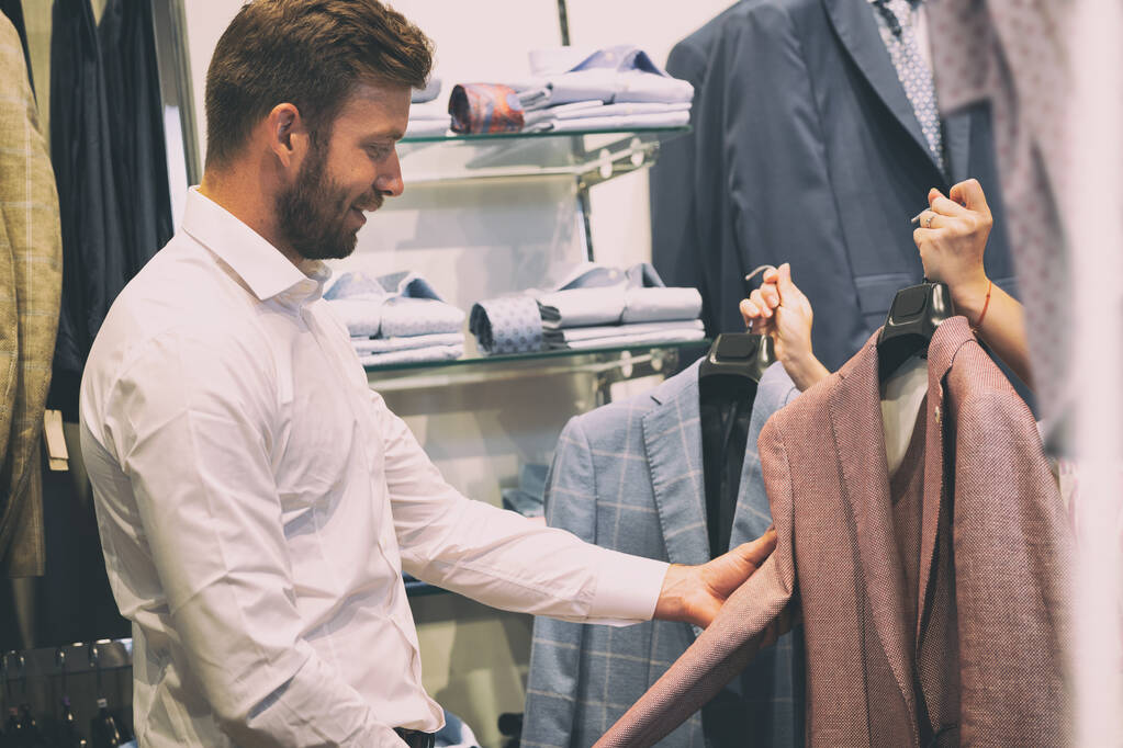 Sprzedawczyni pokazuje dwie kurtki mężczyźnie w sklepie odzieżowym  - Zdjęcie, obraz