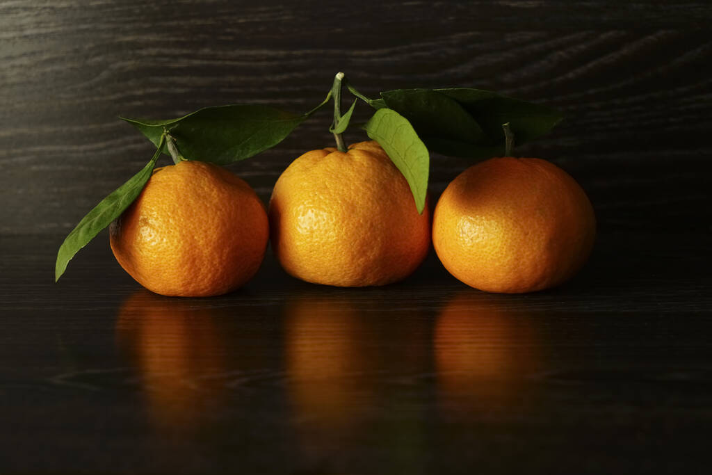 3 frische, reife Mandarinen mit Blättern auf einer Oberfläche aus schwarzem Stein.  - Foto, Bild