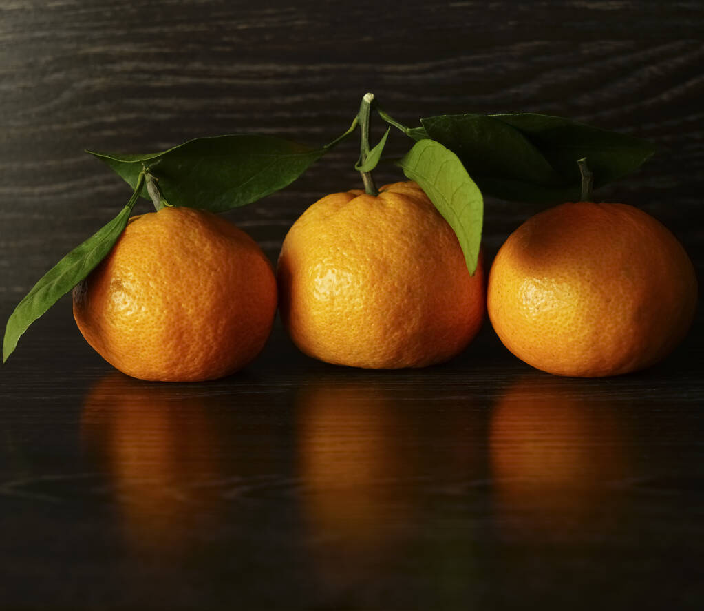 3 tres mandarinas frescas y maduras con hojas sobre una superficie de piedra negra
.  - Foto, imagen