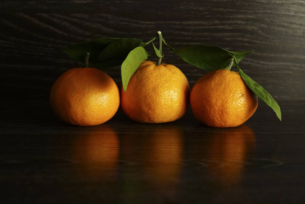 3 tres mandarinas frescas y maduras con hojas sobre una superficie de piedra negra
.  - Foto, Imagen