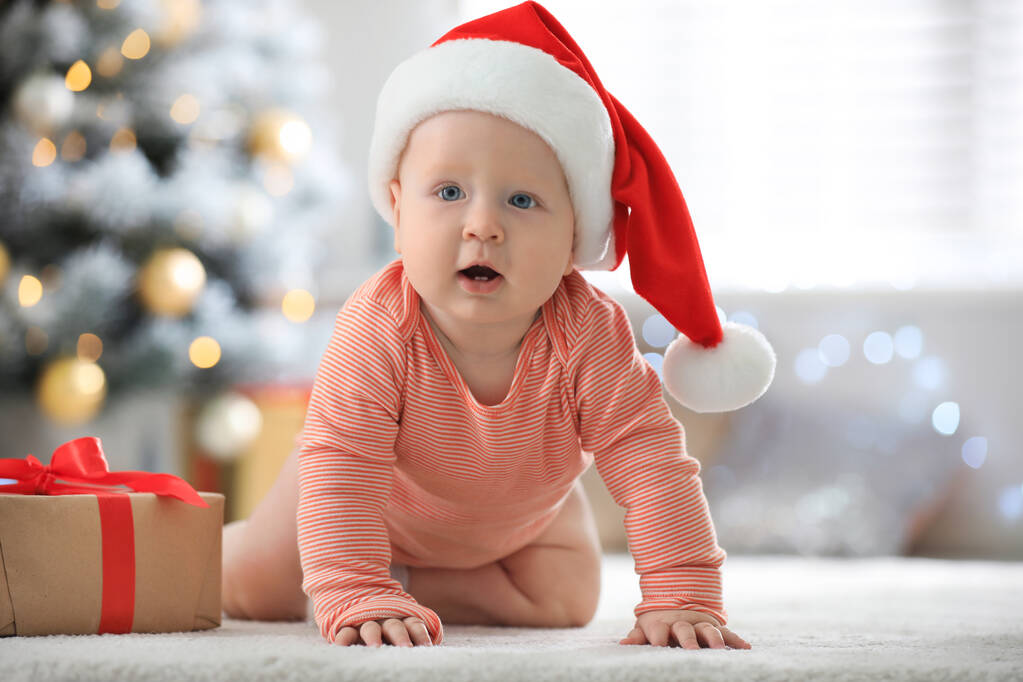 Little baby wearing Santa hat on floor indoors. First Christmas - Photo, Image