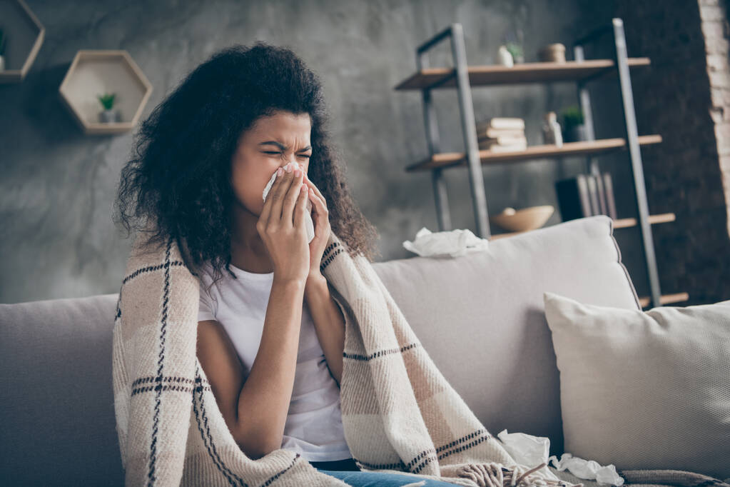 Closeup photo of unhealthy dark skin wavy lady suffering flu caught cold sneezing paper napkins everywhere sitting couch covered plaid blanket living room indoors - 写真・画像
