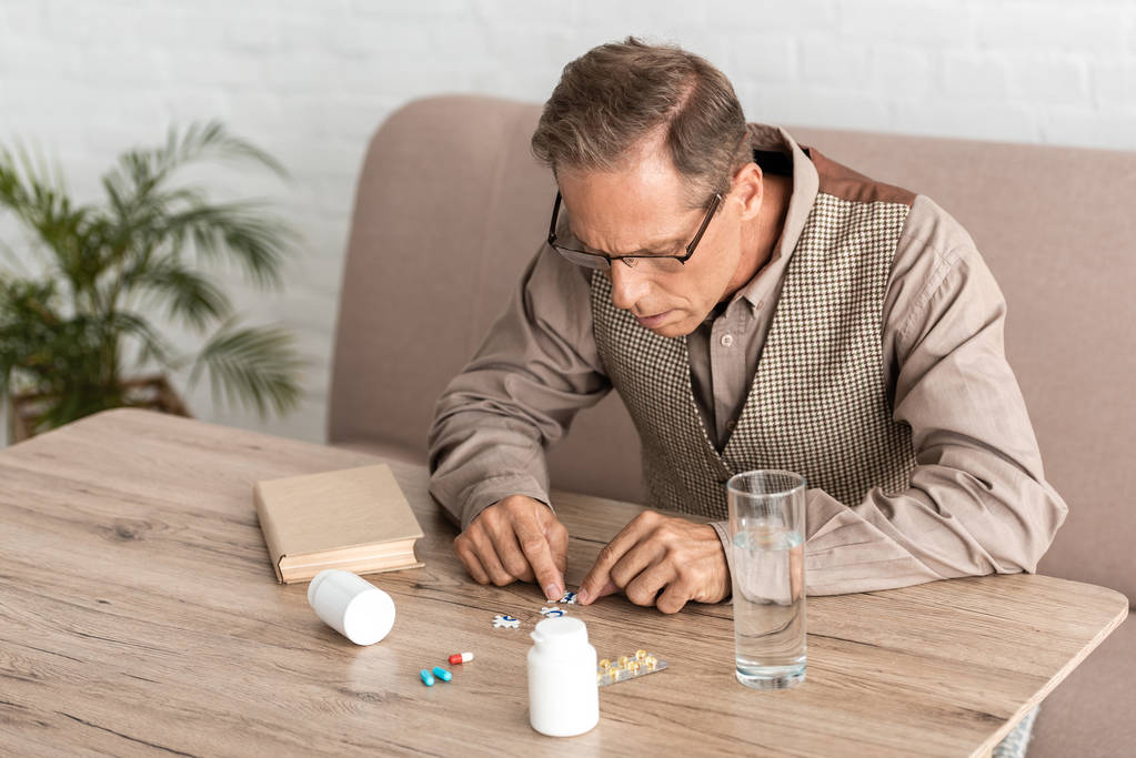gepensioneerde man met Alzheimer die naar pillen op tafel kijkt  - Foto, afbeelding
