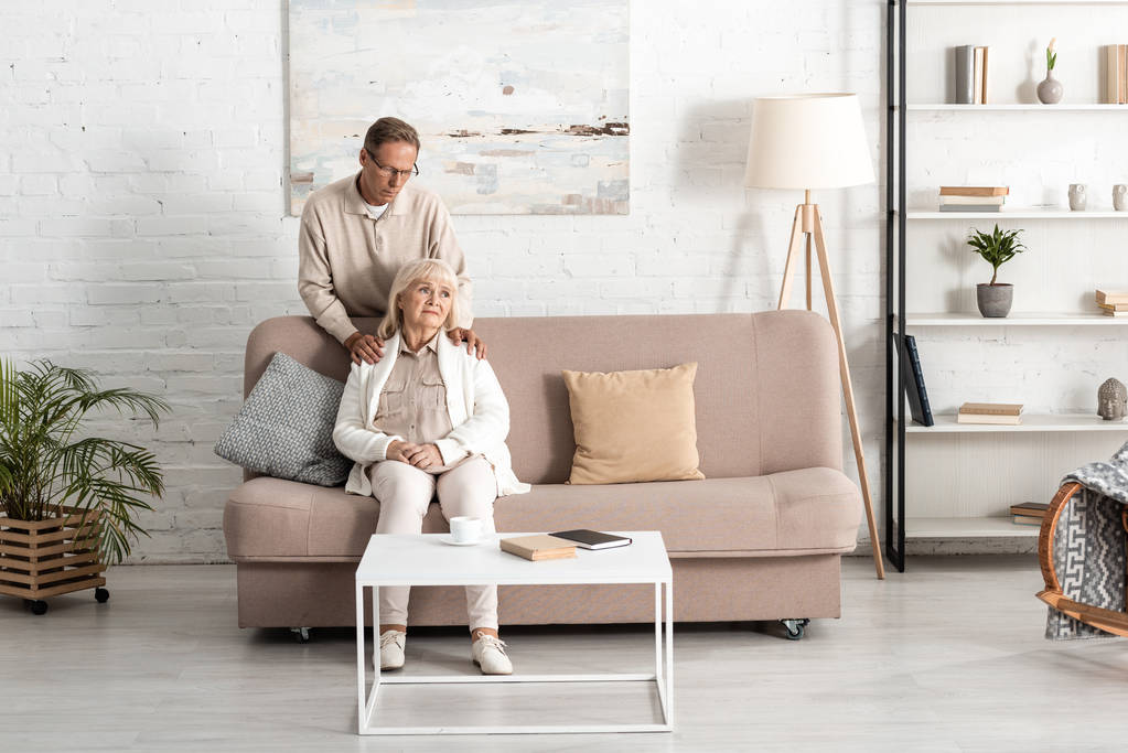 idős férj áll közelében beteg feleség ül kanapén otthon  - Fotó, kép