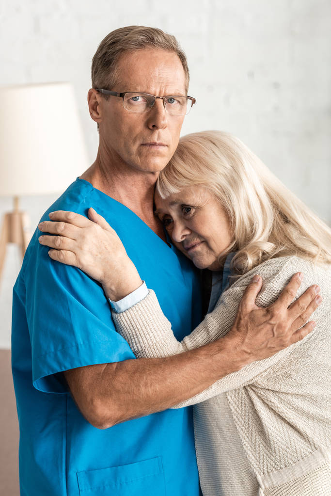 засмучена старша жінка обіймає лікаря в окулярах
  - Фото, зображення