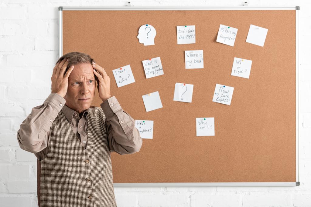 Rentner mit Alzheimer-Krankheit berührt Kopf und steht neben Tafel mit Papieren und Briefen  - Foto, Bild
