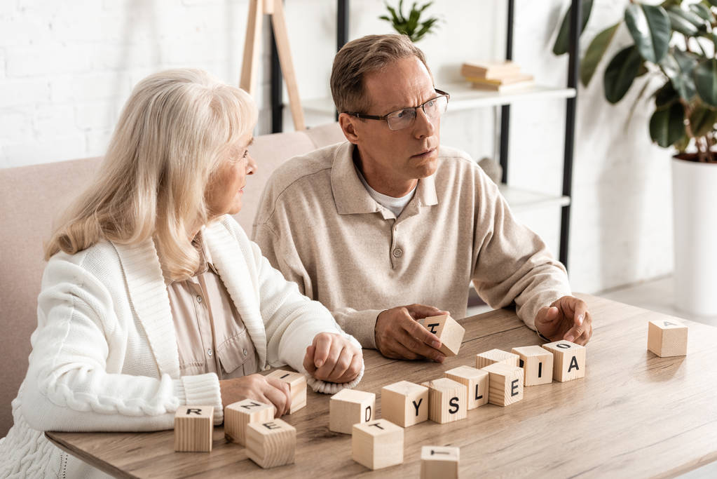 donna anziana guardando marito malato vicino a cubi di legno con lettere di dislessia
  - Foto, immagini