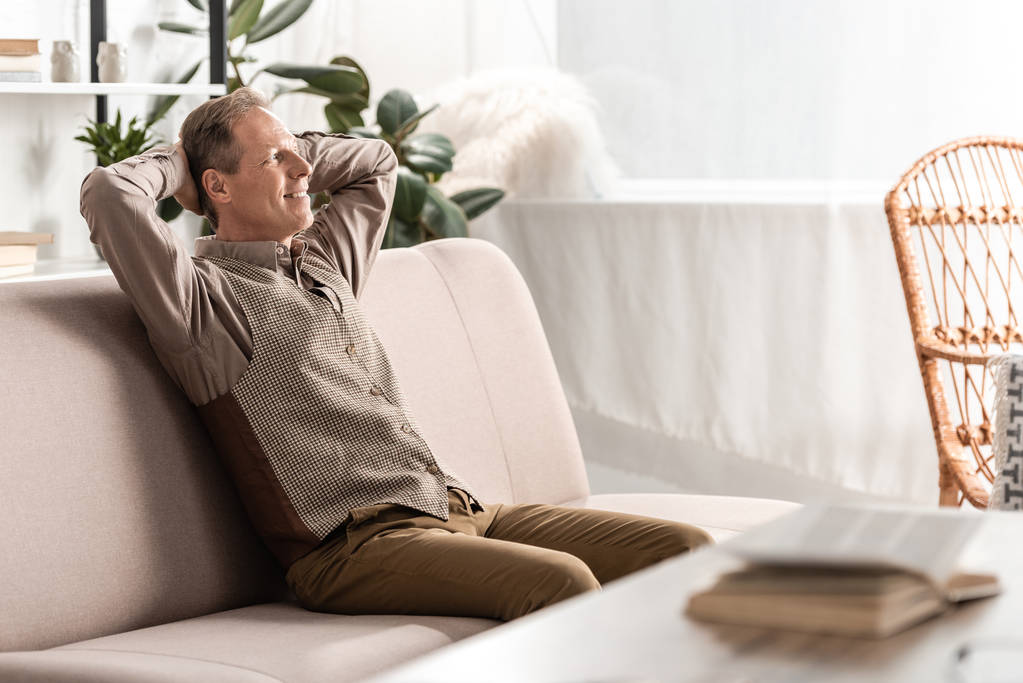 selective focus of cheerful senior man sitting on sofa and gesturing at home  - Photo, Image