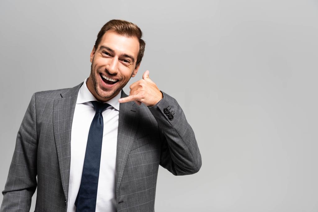 gutaussehender und lächelnder Geschäftsmann im Anzug zeigt Rufzeichen isoliert auf grau  - Foto, Bild