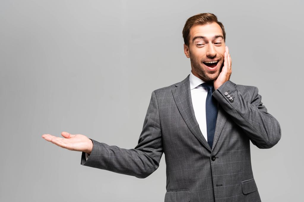 handsome and shocked businessman in suit pointing with hand isolated on grey  - 写真・画像