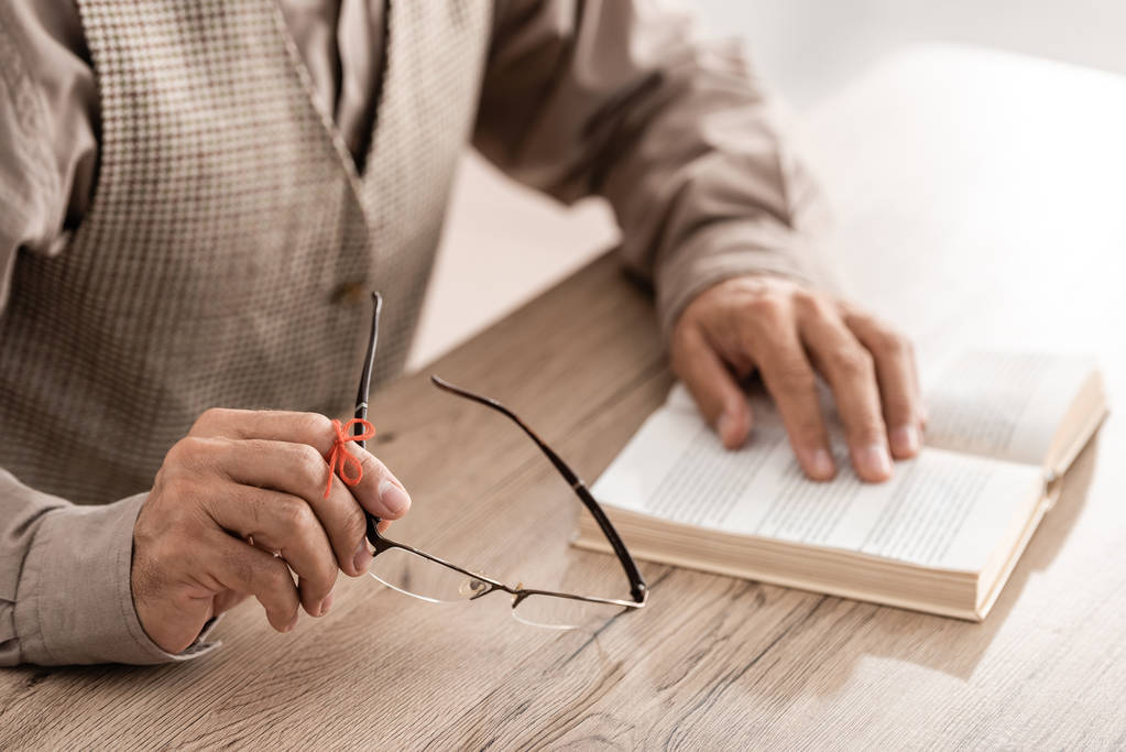 Ausgeschnittene Ansicht eines Rentners mit Alzheimer-Krankheit Zeichenkette menschliche Finger Mahnung hält Brille in der Nähe Buch  - Foto, Bild