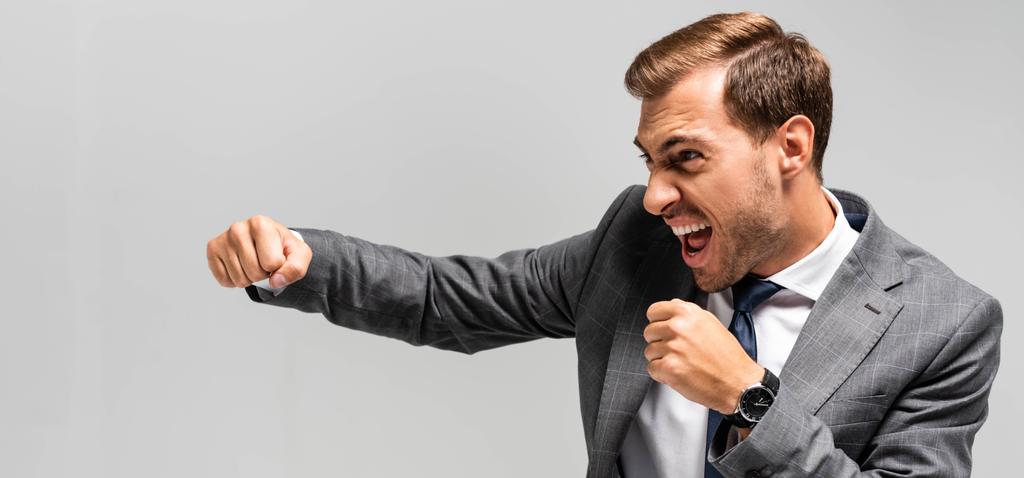 panoramic shot of angry and handsome businessman in suit punching isolated on grey  - Photo, Image