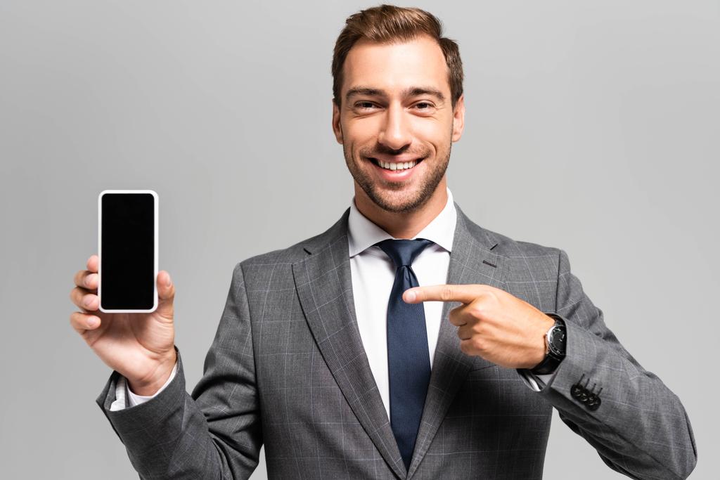 homme d'affaires beau et souriant en costume pointant du doigt le smartphone isolé sur gris
  - Photo, image