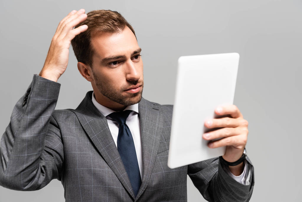 schöner Geschäftsmann im Anzug schaut auf digitales Tablet isoliert auf grau  - Foto, Bild
