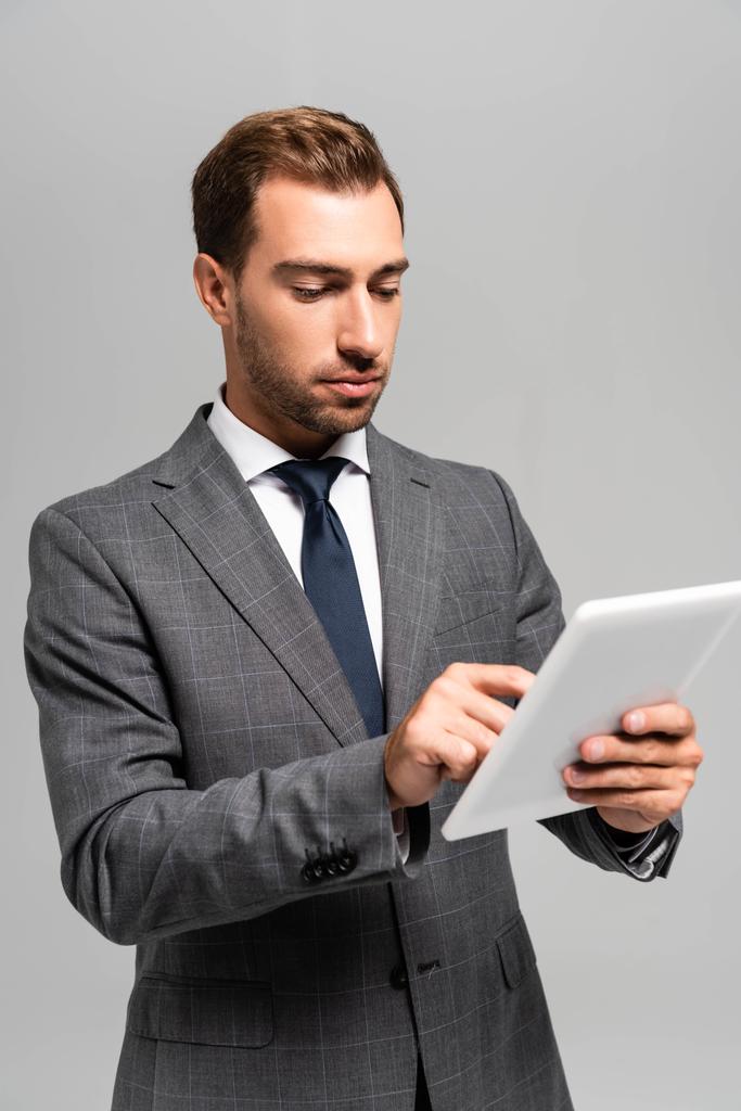 schöner Geschäftsmann im Anzug mit digitalem Tablet isoliert auf grau  - Foto, Bild